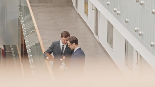 两位成功的商人穿着西装站在当代商业中心的玻璃栏杆旁讨论公司项目 他们的高角速度慢悠悠 — 图库视频影像