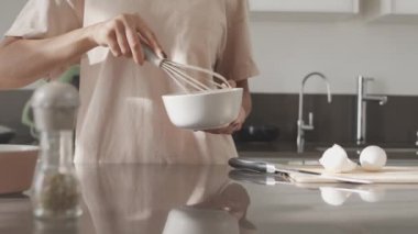 Orta kısımda tanınmayan bir kadının mutfakta çırpılmış yumurta pişirirken yumurtayı çırpması.