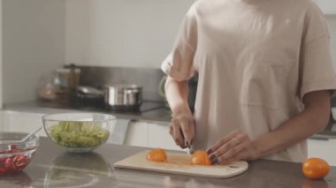 Portakal domateslerini keserken arka planda kaynayan suyla evde sağlıklı öğle yemeği hazırlayan tanınmamış kadının orta bölüm yavaşlaması.