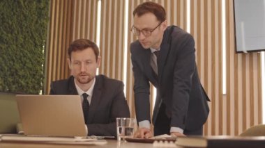 Toplantı odasında iş projelerini tartışırken dizüstü bilgisayar kullanan iki başarılı orta yaşlı beyaz iş adamının orta boy yavaşlaması.