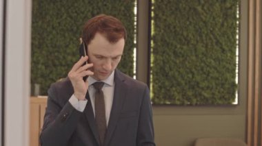 Kendine güvenen, mavi takım elbiseli beyaz iş adamının belini kaldır ve akıllı telefonu içeri al.