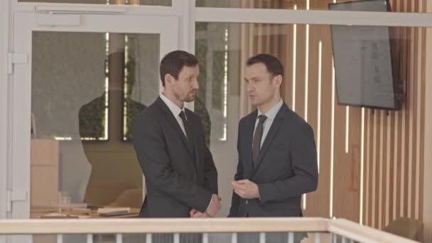 会議室の外で会話をしているスーツとネクタイの2人の自信のあるビジネスパートナーの中低速 — ストック動画