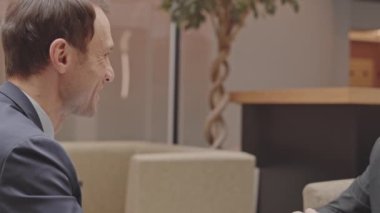 Orta yaşlı iş ortaklarının belini büküp başarılı bir sözleşme imzaladıktan sonra el sıkışmaları, çağdaş iş merkezinde masada oturmaları.