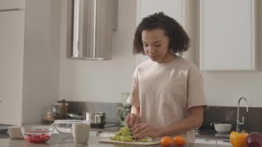 20 'li yaşların başında melez bir kız öğle yemeği için sağlıklı salata yaparken mutfak masasında marul yapraklarını kesiyor.