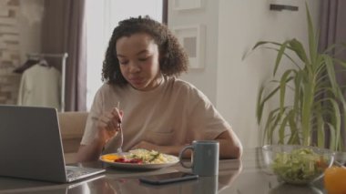 Evde sağlıklı kahvaltı yaparken dizüstü bilgisayarda film izleyen melez kızın belini kaldır.