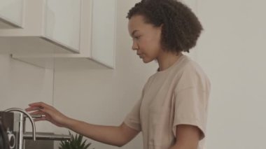 Mutfakta bardakları yıkarken ev işlerini yapan melez bir kadının yavaş yavaş eğilmesini.