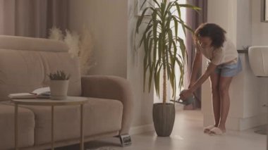 Evdeki ev işlerini yaparken rahat ev kıyafetleri içinde ev bitkilerini sulayan güzel, melez bir kadın.