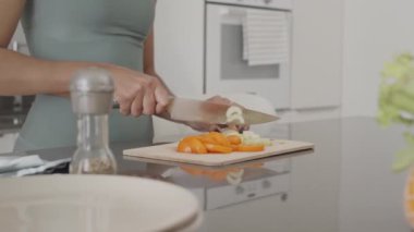Evde sağlıklı bir öğle yemeği hazırlarken güvertede taze sebze kesen tanınmayan fit bir kadının orta bölüm yavaşlaması.