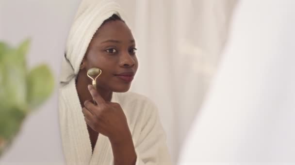 洗完澡后 站在镜子前 用石英滚筒按摩脸部 在肩膀上与慢吞吞的年轻的非洲裔美国妇女保持着中等的亲密接触 — 图库视频影像