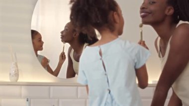 Genç, güzel, siyah bir kadın ve 6 yaşındaki kızının yüz masajı yaparken yüz masajı yaparken kuvars silindiri kullanmasının orta yavaşlığı.