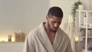 Sabah duşundan sonra sakalına parfüm süren bornozlu yakışıklı Afrikalı Amerikalı genç adam.