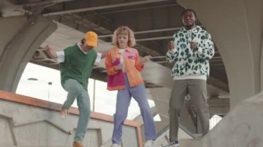 Açık otoparkta serbest dans eden renkli Y2K kıyafetleri içindeki çok ırklı bir grup yavaş ve yavaş arkadaş.