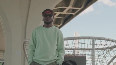 Kırmızı bandanalı Afrikalı Amerikalı hippi çocuk, siyah güneş gözlüğü ve kentsel arka planda kameraya gülümseyen naneli kazak.