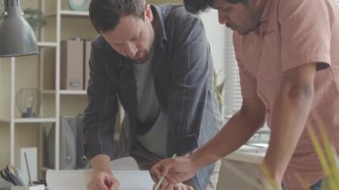 İki çok ırklı mimarın inşaat projesinin taslaklarını ve planlarını tartışırken yavaşlayıp modern mimarlık bürosunun masasında oturuyorlar.