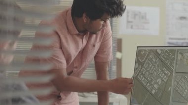 Çift ırklı erkek mühendis, iş planını meslektaşlarına açıklarken şehir haritasını bilgisayar ekranında gösteriyor.