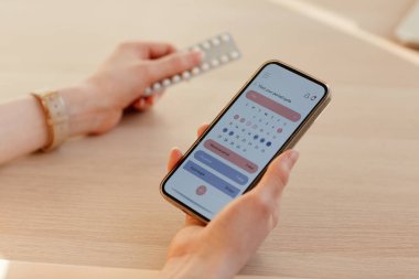 Mobil uygulama ve doğum kontrol hapları kullanarak adet döngüsü hesaplayan genç bir kadın.