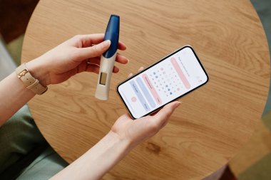 Mobil uygulama kullanarak adet döngüsü hesaplayan ve hamilelik testi yapan genç bir kadın.