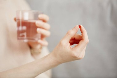 İlaç ya da vitamin alırken elinde hap kapsülü ve bir bardak su tutan genç bir kadının en az yakın çekimi, kopyalama alanı