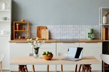 Ön plandaki yemek masasında açık dizüstü bilgisayarı olan beyaz renkli minimal mutfak iç mekanı, boşluğu kopyala
