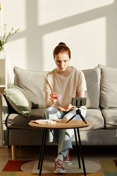 Минимальный портрет кавказской девушки, держащей менструальную чашку перед камерой и снимающей образовательное видео о женских гигиенических средствах, копировальное пространство