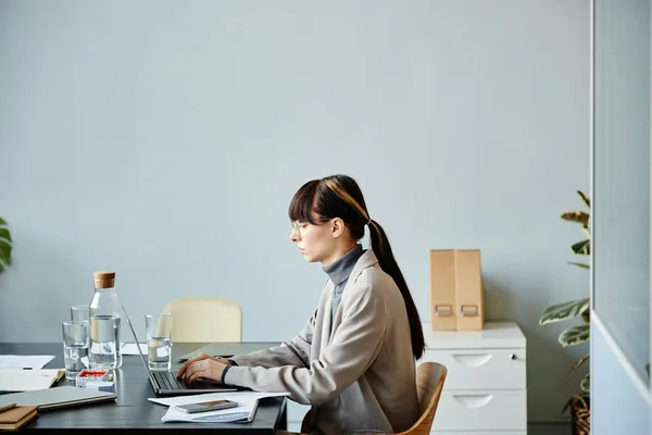 青い壁に対してオフィスの会議テーブルでコンピュータを使用して若い女性の最小側のビューの肖像画 コピースペース — ストック写真