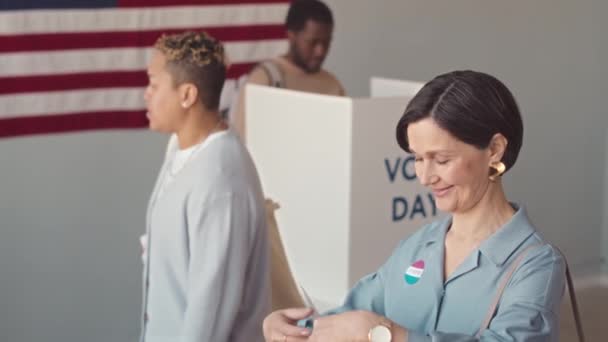中等速度的成熟白人妇女和其他多样化的美国公民站在投票站的桌旁 拿着选票 与在那里工作的人交谈 — 图库视频影像