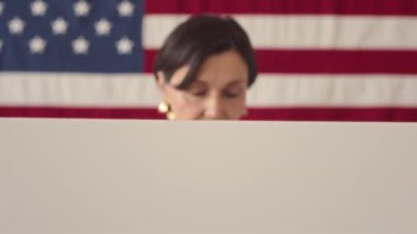 Seçim günü oy kabininde dikilirken kameraya gülümseyen olgun beyaz kadın portresini kaldır