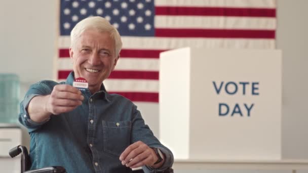 坐在轮椅上的快乐的白种人老年灰发男子的慢镜头画像 显示出我在投票站投票时的贴纸 墙上挂着美国国旗 背景模糊 — 图库视频影像
