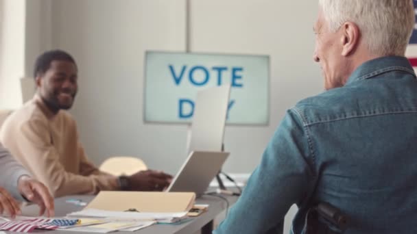 坐在轮椅上的高个子灰发男子坐着轮椅来到地方选举站的办公桌前投票的后视镜 来到这里就美国选举进行投票 — 图库视频影像