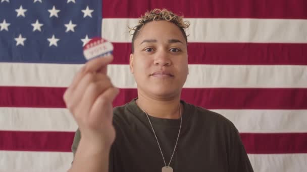 站在投票站 站在美国国旗前的年轻女军人面带微笑地举起慢镜头 并在镜头前展示投票贴纸 — 图库视频影像