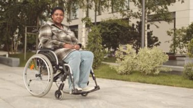 Özürlü genç Afrikalı kadının tam boy yavaş portresi. Yaz günü tekerlekli sandalyede otururken kameraya gülümsüyor.