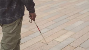 Gündüz vakti kaldırımda yürürken baston kullanan tanınmayan kör bir adamın ağır çekimleri.