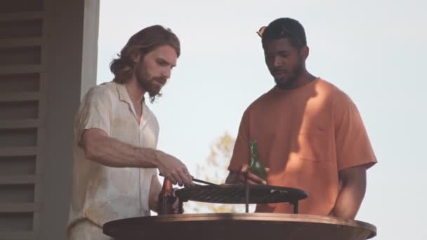 两个多民族男性朋友站在烤肉烤架边喝啤酒聊天时的慢动作 — 图库视频影像