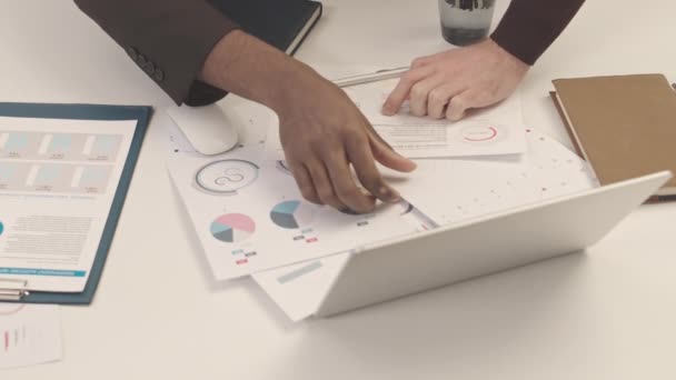 企業プロジェクトの予算を計画しながら オフィスの机で印刷された財務グラフやチャートを見て2人の多民族の若いビジネスマンの減速を傾ける — ストック動画
