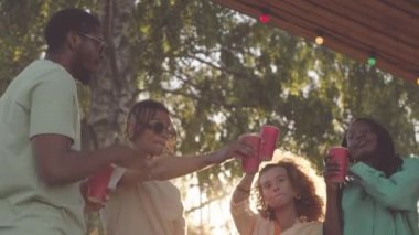 Düşük açılı orta yaşlı, kırmızı bardaklı altı genç arkadaş Summerhouse partisinde müzik eşliğinde dans ediyor.