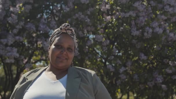 공원에서 꽃피는 라일락 나무에 기대어 아프리카 미국인 여성이 모습을 느림보 — 비디오
