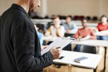 Erkek üniversite profesörünün sınıfta öğrencilere ders verirken notları kontrol etmesi, kopya alanı