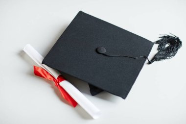 Mezuniyet şapkası ve diplomasını beyaz arka planda kırmızı kurdeleyle kapat