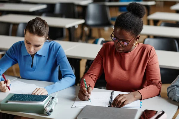 アフリカ系アメリカ人の若い女性がノートを取りながら 大学の教室で机の上で勉強 — ストック写真