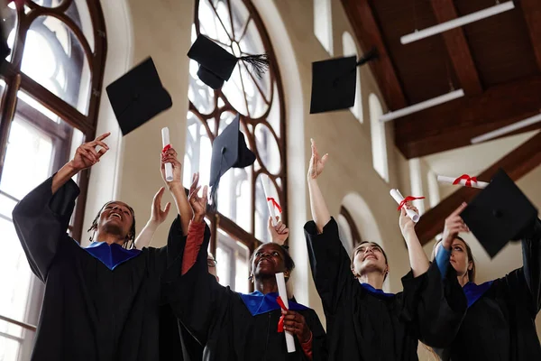 大学の卒業式で卒業生のガウンを着用し 空気中のキャップを投げる喜びの若者のグループ — ストック写真