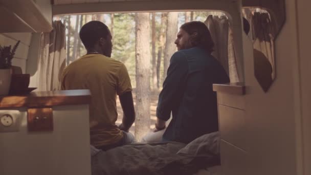 リアビュー中出しの二人の若いです多様な男性友人座っていますベッドの上に居心地の良い家で車輪の上で会話 — ストック動画