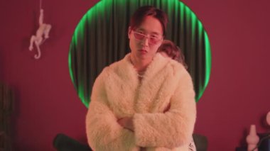 Modaya uygun hipster Asyalı bir çocuk ve göz alıcı kıyafetler içindeki üç güzel kız retro stüdyosundaki neon ışıklarıyla vogue hareketlerini gösteriyor.