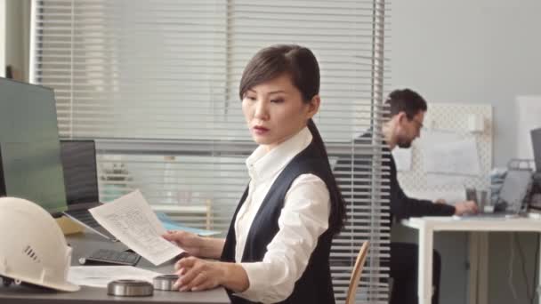 一位严肃的年轻亚洲女性设计工程师坐在办公室的电脑前与男性同事一起工作 一边看着设计图 一边慢慢等着你 — 图库视频影像