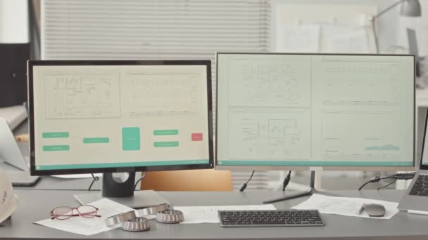 現代のオフィスで設計エンジニアの作業机の上に画面上の技術スキームを持つ2台のコンピュータモニタの遅い人はいません — ストック動画