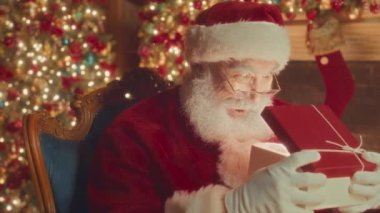 Waist up slowmo portrait of surprised bearded Santa opening beautiful Christmas present box and looking at camera
