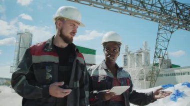 Medium shot of two multiethnic workers talking while walking along industrial site outdoors