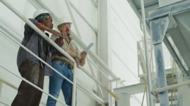 Low angle shot of multiethnic couple of professional factory workers discussing plan of work at granite processing plant