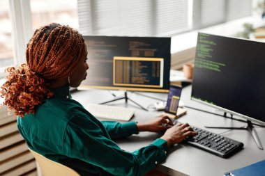 Ofis içi çalışırken bilgisayar ekranında programlama kodu ile klavyede yazan kadın IT geliştiricisinin yan görünümü, boşluk kopyala