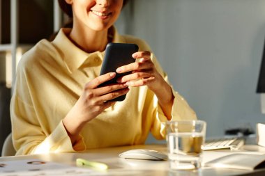 Orta bölüm, bej gömlekli genç bir kadını ofis odasında otururken akıllı telefondan mesaj atarken çekmiş.