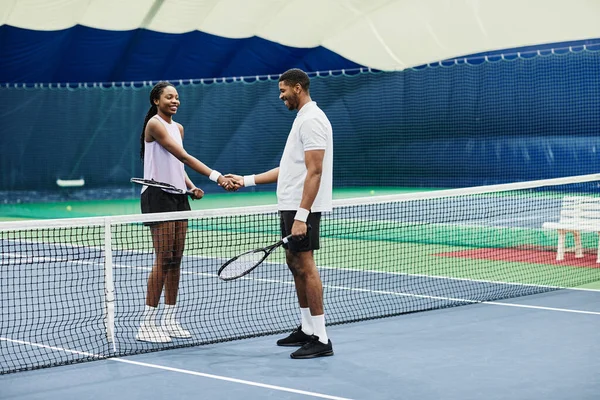 屋内コートで試合中にネット上で握手2人のテニス選手の完全な長さのショット コピースペース — ストック写真